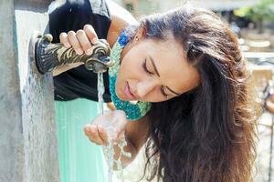 Porträt von ziemlich Mädchen Getränke Wasser von Quelle im Sommer- Stadt foto