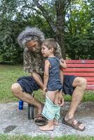 Mitte alt Papa Ändern kurze Hose zu seine Sohn im ein draussen Park foto