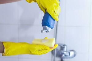 Frau im Handschuhe Putten Reinigung Chemie zu das Schwamm und wollen zu sauber oben das Badezimmer foto