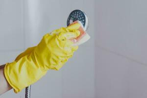 Frau im Gummi Handschuhe Reinigung das Dusche Kopf. Hausmädchen Waschen metallisch Kopf von das Dusche. Hausfrau Reinigung oben im das Badezimmer foto