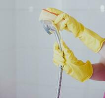 Frau im Gummi Handschuhe Reinigung das Dusche Kopf. Hausmädchen Waschen metallisch Kopf von das Dusche. Hausfrau Reinigung oben im das Badezimmer foto