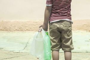 Plastik Verschmutzung auf Land. wenig Junge Sammeln Plastik Flaschen. Kind tragen Müll Tasche. kostenlos Raum foto