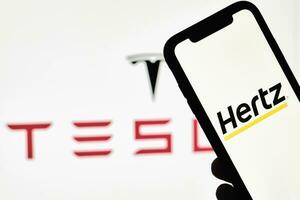 ein Person hält Smartphone mit Hertz Warenzeichen Über groß Tesla Logo foto