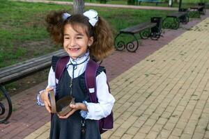 Mädchen mit Rucksack Essen Sandwich verpackt im ein Sandwich Box in der Nähe von Schule. ein schnell Snack mit ein Brötchen, ungesund Essen, Mittagessen von Schule. zurück zu Schule. Ausbildung, primär Schule Klassen, September 1 foto