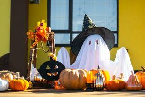 Kind im Bett Blatt mit Schlitze mögen Geist im Hexe Hut und Halloween Dekor auf das Veranda von das Haus draußen im das Hof von Kürbis, Laterne, Girlanden, ack Laterne. Party, Herbst Stimmung foto