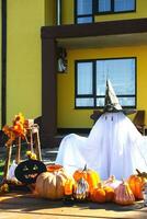 Kind im Bett Blatt mit Schlitze mögen Geist im Hexe Hut und Halloween Dekor auf das Veranda von das Haus draußen im das Hof von Kürbis, Laterne, Girlanden, ack Laterne. Party, Herbst Stimmung foto