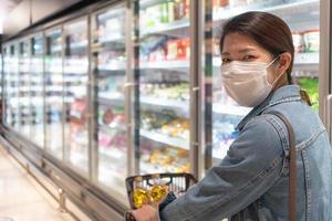 junge Asiatin mit Maske beim Einkaufen von Lebensmitteln im Supermarkt foto