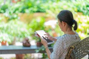 Senior asiatische Frau mit Tablet, um Social Media im Hausgarten zu spielen.