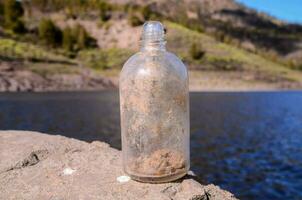 ein Flasche mit Schmutz auf es Sitzung auf ein Felsen in der Nähe von ein See foto