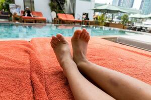 Sonnenbaden durch das Hotel Tourist Hotel Schwimmen Schwimmbad, mans Beine Lügen Nieder auf ein Sonnenliege suchen Über das Wasser foto