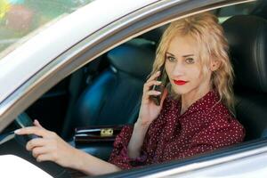 Porträt von ein schön blond Frau im ein rot Kleid Sitzung im ein Auto mit ein Telefon foto