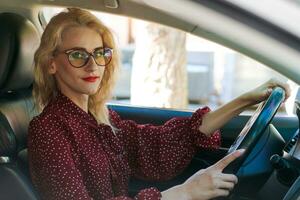 schön erfolgreich blond Frau im ein rot Kleid Sitzung im ein Auto hinter das Rad foto