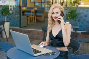 schön Frau im Brille sitzt beim Tabelle im ein Straße Cafe und funktioniert auf Tablette foto