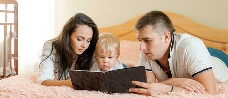 glücklich Familie Lügen auf das Bett lesen ein Buch, Mama Papa und wenig Sohn, Banner foto