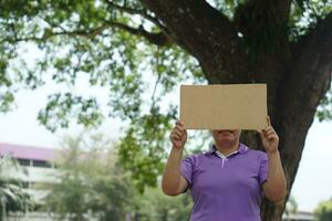 Frau halt leer Papier Plakat zum Hinzufügen Wörter oder Text, Stand unter das Baum. Konzept, Kampagne Zeichen und Notiz. Bekanntmachung. geben Information. foto