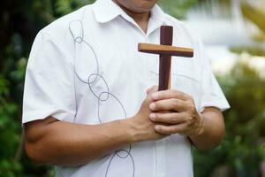 Nahansicht asiatisch Mann Christian hält hölzern Kreuz und betet draussen . Konzept , Christian Verehrung. Glaube, Vergebung, Glaube, Liebe und Hoffnung. religiös Symbol von Christentum. foto