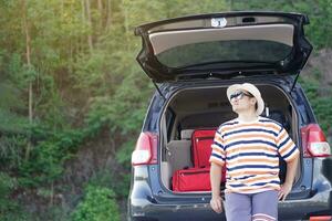 asiatisch Mann Reisender sitzen auf Kofferraum von Auto mit Koffer. Konzept, entspannen Zeit. Ferien oder Urlaub Ausflug durch Privat Fahrzeug. Transport. geben Zeit zum du selbst. foto