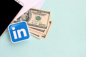 Linkedin Papier Logo Lügen mit Briefumschlag voll von Dollar Rechnungen und Smartphone foto