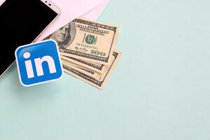 Linkedin Papier Logo Lügen mit Briefumschlag voll von Dollar Rechnungen und Smartphone foto