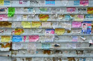 Charkow, Ukraine - - Juni 24, 2018 Grunge Botschaft Tafel mit viele Werbung. Menschen Verbreitung Werbung und Information auf Weiß Papier als Post es auf Metall Zaun foto