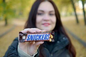 Charkow, Ukraine - - Oktober 8, 2019 ein jung kaukasisch Brünette Mädchen zeigt an kichert Schokolade Bar im Herbst Park. kichert Schokolade hergestellt durch Mars foto