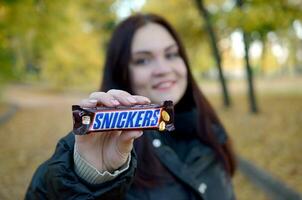 Charkow, Ukraine - - Oktober 8, 2019 ein jung kaukasisch Brünette Mädchen zeigt an kichert Schokolade Bar im Herbst Park. kichert Schokolade hergestellt durch Mars foto