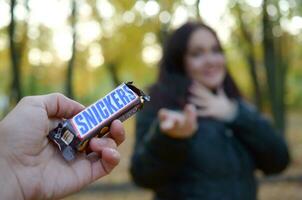 Charkow, Ukraine - - Oktober 8, 2019 männlich Hand geht vorbei das Mädchen ein kichert Schokolade Bar im ein Herbst Park. das Manifestation von Freundlichkeit foto