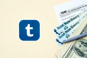 tumblr gedruckt Logo Lügen mit 1040 Individuell Einkommen MwSt Rückkehr bilden mit Rückerstattung prüfen und hundert Dollar Rechnungen auf Beige Hintergrund. Hilfe im MwSt Zeitraum von Sozial Netzwerk Konzept foto