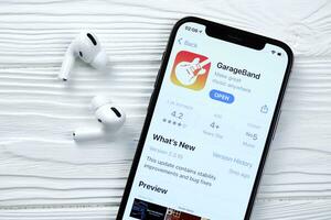 Charkow, Ukraine - - März 5, 2021 Garageband zum Künstler Symbol und Anwendung von App Geschäft auf iPhone 12 Profi Anzeige Bildschirm mit Airpods Profi auf Weiß Tabelle foto