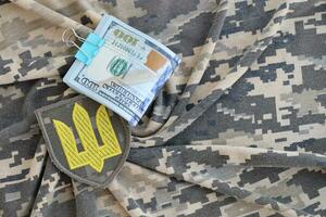 ukrainisch Heer Symbol und Bündel von Dollar Rechnungen auf Militär- Uniform. Zahlungen zu Soldaten von das ukrainisch Heer von vereinigt Zustände, Gehälter zu das Militär. Krieg Unterstützung foto