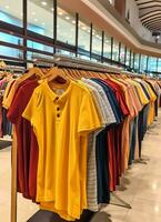 Reihe von modisch Polo T-Shirts zum Mann auf hölzern Aufhänger oder Gestell im ein Kleidung Boutique Verkauf Geschäft Konzept durch ai generiert foto