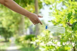 asiatisch Frau wirft Plastik Wasser Flasche nach Trinken alle das Wasser auf zu das Seite von das Straße im ein Park foto