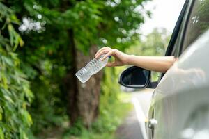 Frau Hand werfen Weg Plastik Flasche von Auto Fenster auf das Straße im Grün Natur foto