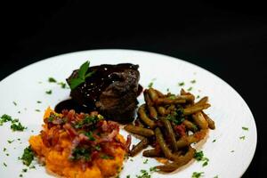Kalbfleisch Wangen mit Süss Kartoffel Püree und Speck mit Bohnen im Tomate Soße und Knoblauch foto