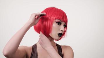 junge Frau, die ihr kurzes glänzendes gefärbtes Haar mit Kamm stylt, Pflegekonzept, rote Haarperücke kämmt, 4k foto