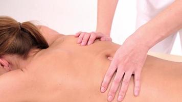 junge Frau mit Massage im Spa-Salon. Nahaufnahme der Frau, die sich während der Rückenmassage auf dem Massagetisch in Zeitlupe entspannt.