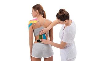 Physiotherapeut, der Kinesio-Tape auf den unteren Rücken der Patientin anwendet. Kinesiologie, Physiotherapie, Rehabilitationskonzept. foto
