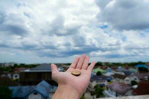 einer Hand hält ein Münze. zu Show seine verwenden von Geld das Hintergrund ist das Stadt. und das Blau Himmel Abdeckungen foto