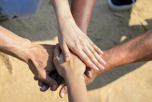 Gruppe von Vielfalt Freiwillige Menschen tun gestapelt Hände Unterstützung zusammen während tun Nächstenliebe Aktivität draußen auf das Strand foto