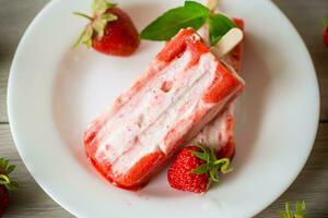 hausgemacht Erdbeere Eis Sahne auf ein Stock im ein Teller mit Erdbeeren foto