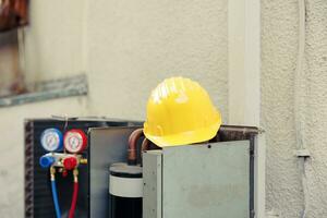 schließen oben von Gelb Schutz Helm auf oben von aus von Bedienung extern Luft Conditioner Einheit im brauchen von Reparatur. draussen geöffnet hvac System mit Verteiler Messgeräte und Sicherheit Ausrüstung foto