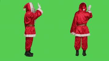 glücklich Santa claus Welle Hallo im Studio, tragen festlich Kostüm mit Brille und rot Hut Über voll Körper grüner Bildschirm. Heilige Nick Gruß jemand und Verbreitung Ferien Geist. foto
