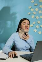korporativ Mitarbeiter mit Schmerzen von zervikal Verletzung tragen medizinisch Halsband Sitzung beim Schreibtisch im modern Büro. Fachmann Frau Arbeiten mit Laptop mit Ausdruck von Müdigkeit und leichte Schmerzen. foto