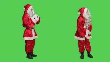 Santa Cosplay Überprüfung Zeit auf Armbanduhr, Stehen Über voll Körper grüner Bildschirm im Studio. Vater Weihnachten tragen berühmt rot Kostüm mit Weiß Bart, Schauspielkunst ungeduldig auf Kamera. foto