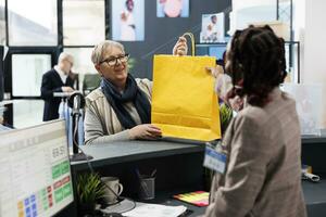 Senior Shopaholic Frau nehmen Einkaufen Taschen, Herstellung Kauf beim Kasse registrieren im Kleidung speichern. Alten Klient Kauf elegant formal tragen im modern Boutique. kommerziell Aktivität Konzept foto