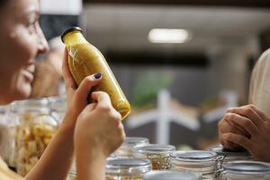 Verkäufer präsentieren ihr Produkte im Null Abfall Marktplatz Veranstaltungsort, Verkauf hausgemacht Obst Saft zu interessiert Kunde, schließen hoch. lokal Farmer Handel gesund Essen Artikel während Fall, verschwommen Hintergrund foto