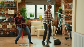 afrikanisch amerikanisch Partner Hören zu Musik- und Waschen Böden im Leben Zimmer, tun dumm komisch tanzen bewegt. heiter Menschen tun Frühling Reinigung und Tanzen im Wohnung, wischen. foto