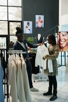 schwanger Frau Einkaufen zum Mutterschaft Kleider im modern Boutique, Arbeiter Portion Klient mit das richtig Shirt. afrikanisch amerikanisch Kunde Kauf modisch Fan-Shop im Kleidung Geschäft foto