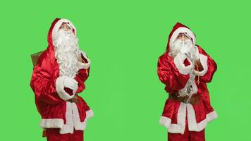 Vater Weihnachten zeigt an stumm Symbol, ausdrücken Privatsphäre und Stille Über grüner Bildschirm im Studio. Santa claus mit Geschenke Tasche tun Stille Zeichen zu behalten Geheimnis, Privat saisonal Winter Charakter. foto