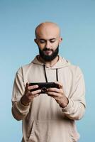 arabisch Mann mit Smartphone Anwendung und spielen Video Spiel während Freizeit Aktivität. jung lächelnd Person halten Handy, Mobiltelefon Telefon im Vertikale Modus und Aufpassen Video online foto